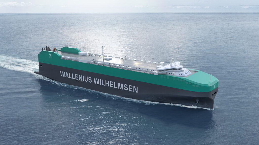 A large cargo ship with a green and black hull is sailing on calm ocean waters. The ship is labeled "WALLENIUS WILHELMSEN" on its side.